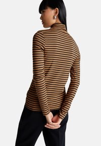 Braun gestreiftes Rollkragenshirt mit langen Ärmeln und taillierter Silhouette, kombiniert mit schwarzen Hosen. Glatter, elastischer Stoff.