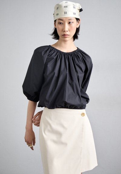 Black, puff-sleeve top with elastic neckline paired with a beige skirt featuring a button detail. Smooth fabric in a fitted silhouette.
