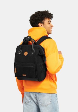 Sac à dos en velours côtelé noir avec poignet supérieur et bretelles ajustables. Comprend une poche zippée à l'avant et un emblème de la marque à l'avant. Design durable.