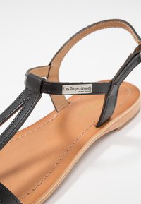 Sandalo in pelle nera con sottili cinturini, design con punta aperta e sottopiede imbottito in marrone chiaro con cuciture a contrasto. Dettaglio del marchio in argento.