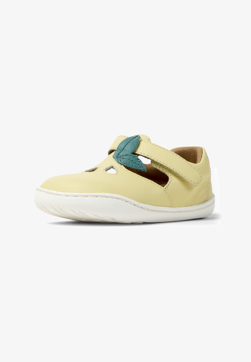 Zapato de cuero amarillo con detalles recortados, con un acento en forma de hoja en color verde azulado en la correa y una suela de goma blanca. Textura suave y forma redondeada.