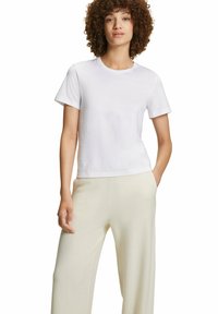 Maglietta bianca in cotone a maniche corte, con scollatura a girocollo e vestibilità rilassata, abbinata a pantaloni beige chiaro a gamba larga.