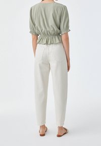 Haut vert clair à manches courtes avec taille froncée et pantalon blanc, fuselé. La tenue présente un tissu texturé et des sandales plates.