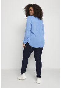 Hellblaues langärmliges Hemd mit lockerer Passform, Rückennähten, kombiniert mit dunklen Skinny-Jeans und weißen Sneakers.