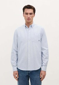 Lichtblauw gestreept overhemd met lange mouwen, een klassieke kraag en een borstzak met een logo-detail. G gedragen met donkere jeans.