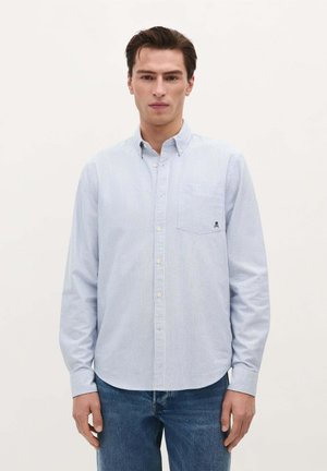 Lichtblauw gestreept overhemd met lange mouwen, een klassieke kraag en een borstzak met een logo-detail. G gedragen met donkere jeans.