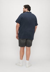 Camisa de manga corta azul marino con rayas verticales blancas, combinada con pantalones cortos oscuros y zapatillas blancas. Tela cómoda y diseño de corte relajado.