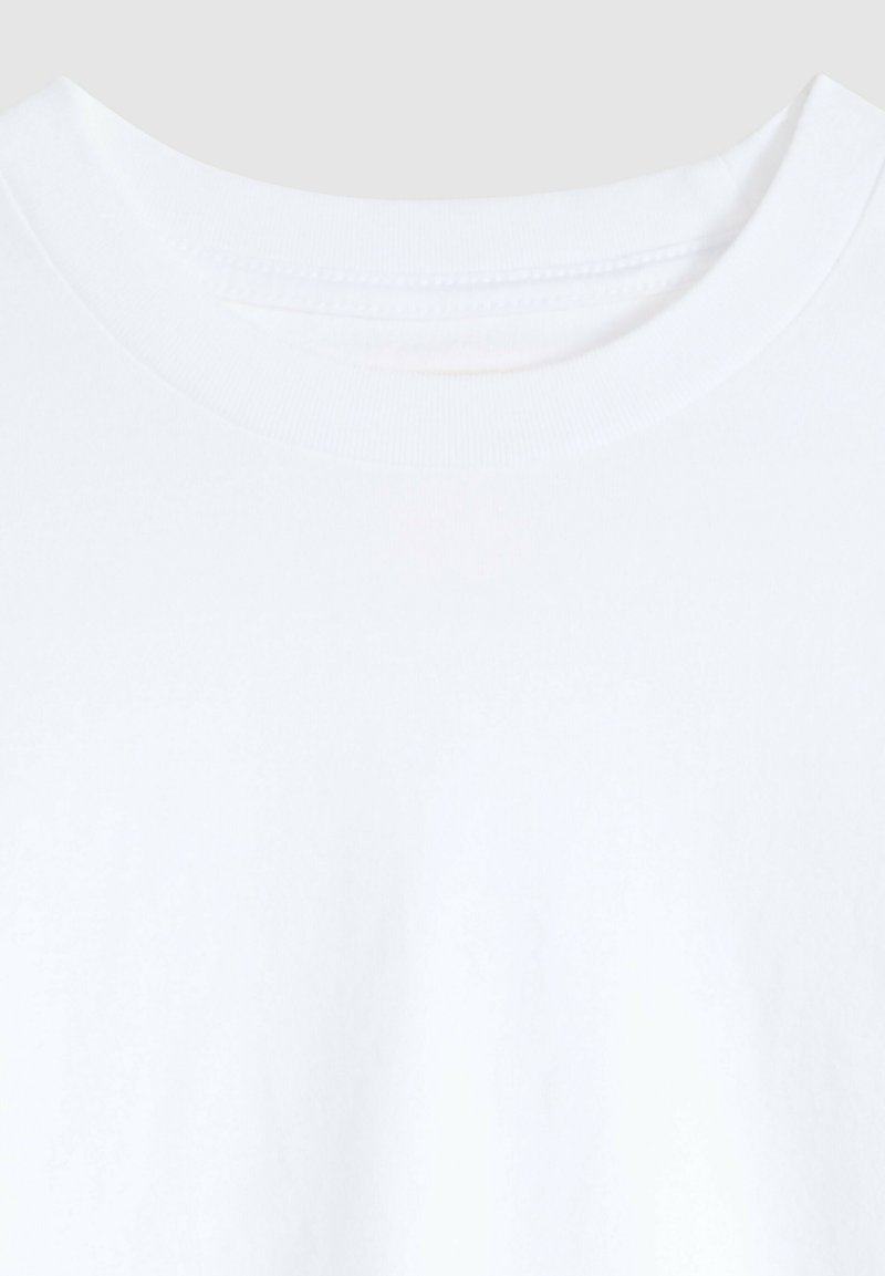 Hvid t-shirt med rund halsudskæring, der viser øverste bryst og rund hals med synlige syninger på ensfarvet baggrund.