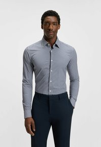 Napapaita avattavalla nappilistalla, jossa on tummansininen ja valkoinen ruutupatterni, pitkät hihat, kaulus ja kiinteä muotoilu. Yhdistetty tummiin housuihin.