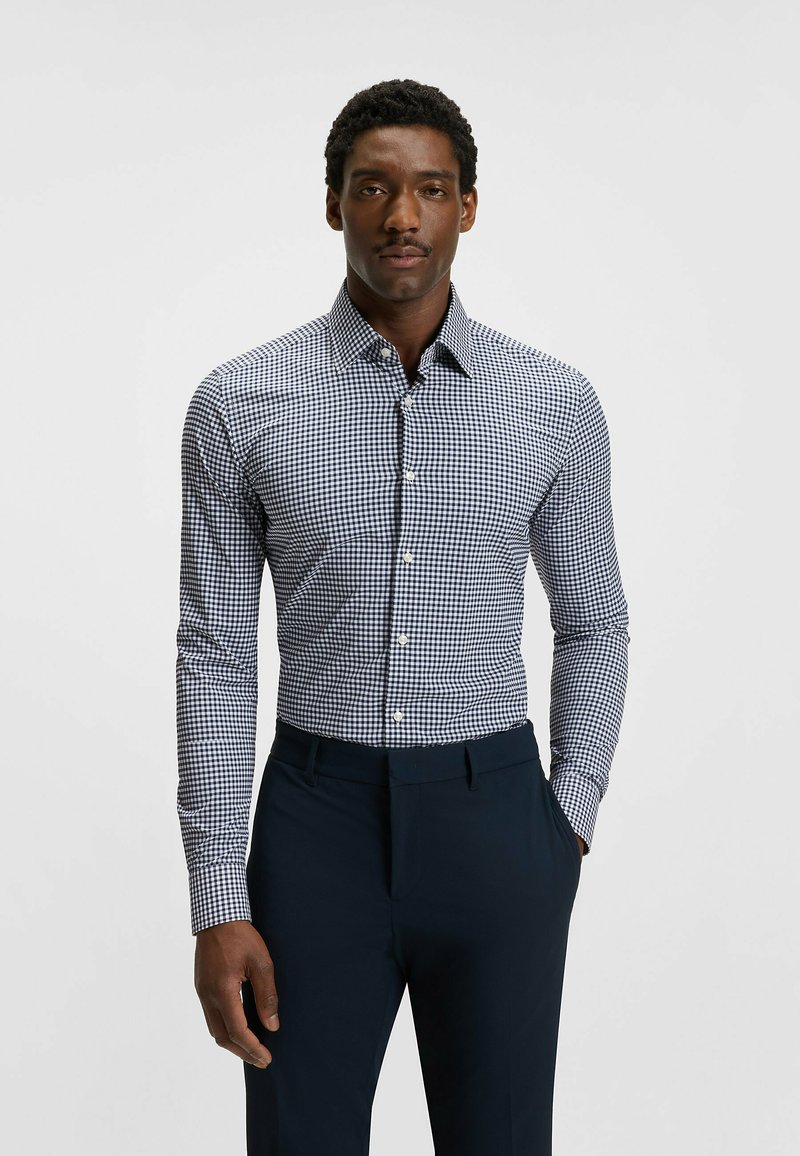 Napapaita avattavalla nappilistalla, jossa on tummansininen ja valkoinen ruutupatterni, pitkät hihat, kaulus ja kiinteä muotoilu. Yhdistetty tummiin housuihin.