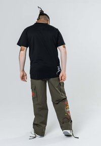 Czarna bawełniana koszulka i oliwkowe spodnie cargo z haftem na czerwono-żółtego tygrysa, z bocznymi kieszeniami i regulowanymi sznurkami przy mankietach.