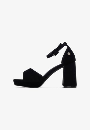 Sandalias de tacón alto de ante negro con un tacón ancho de bloque, tira frontal con punta abierta y una correa en el tobillo con detalle de hebilla.