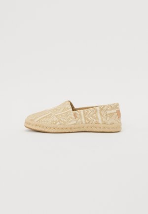 Geflochtene Slipper aus einem beige und cremefarbenen gemusterten Stoffoberteil, kontrastiert durch eine geflochtene Jutesohle und einem kleinen Lederelement.