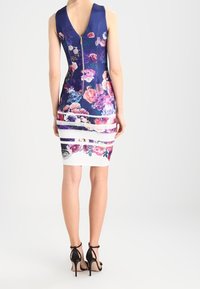 Robe moulante à motif floral avec un col en V, fermeture zip au dos et accents rayés blancs à l'ourlet. Sandales à talons noirs avec lanières complètent le look.
