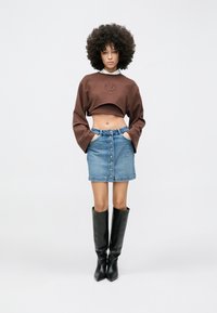 Sudadera marrón corta con detalle bordado, falda vaquera azul con botones delanteros y botas negras de cuero hasta la rodilla. Atuendo casual.