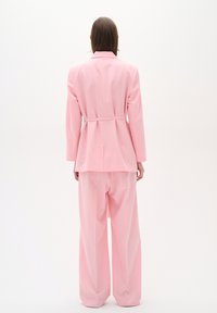 Rozā pielāgota blazer ar jostas vietu, apvienots ar brīviem rozā biksēm; gluda tekstūra, strukturēts dizains un minimālistisks stils.