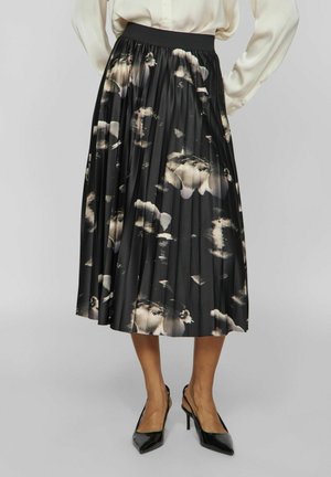 Sort plisseret midi-nederdel med abstrakt beige blomsterprint, båret med cremefarvet bluse og sorte spidse høje hæle.