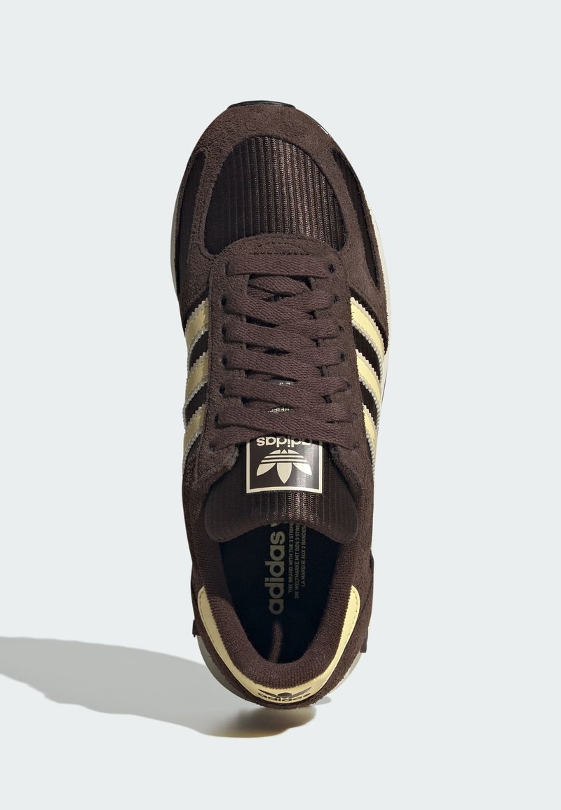 Baskets en daim marron avec des rayures beige, une texture côtelée sur l'orteil, et une étiquette noire de marque sur la languette.