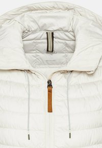 Lichte, gerecycleerde pufi jas in off-white met een hoge kraag, een rits aan de voorkant en een contrasterende bruine ritslip met elastische trekkoorden.