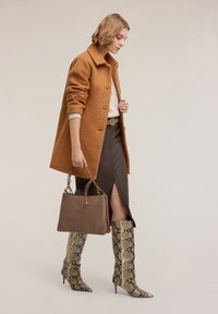 Brązowy płaszcz z teksturą, jasny dzianinowy top, brązowa skórzana spódnica z rozcięciem, botki na wysokim obcasie w wzór węża oraz brązowa torebka na ramię.