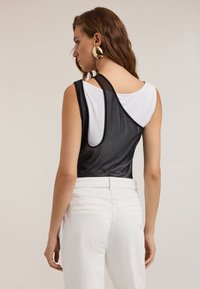 Body in bianco e nero senza maniche con schiena trasparente, abbinato a pantaloni bianchi a vita alta; presenta una texture liscia e un design semplice.