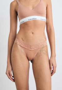 Bralette Calvin Klein en tissu doux et rose avec une bande logo. Le string assorti présente une bordure en dentelle délicate à la taille, avec une finition lisse dans l'ensemble.