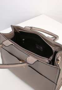 Borsa a mano grigia con texture, dotata di due manici superiori, dettagli in metallo dorato e tasca interna con zip. La borsa presenta un design strutturato.