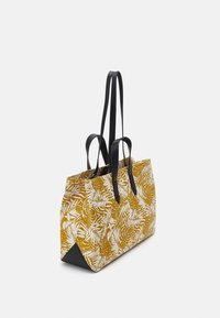 Sac fourre-tout jaune avec un motif de feuilles blanches, doté de poignées en cuir noir et d'une forme rectangulaire structurée. Détail de surface texturée.