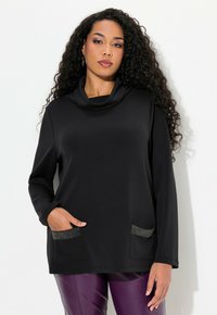 Top negro con cuello cowl en material suave que cuenta con mangas largas, dos bolsillos frontales con acentos metálicos y un ajuste relajado.
