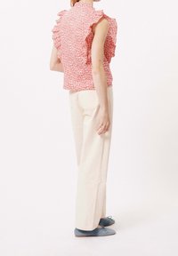 Bluse mit floralem Muster und Rüsche in Rot, kombiniert mit cremefarbenen, weit geschnittenen Hosen und blauen Ballerinas, aus texturiertem Stoff und mit tailliertem Schnitt.