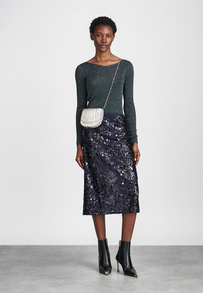 Mirdzoša zaļa krekla garām piedurknēm, tumši zila mirdzoša svārku, un melni potītes zābaki ar zelta akcentiem; pārī ar mazu sudraba pērlīšu crossover somiņu.