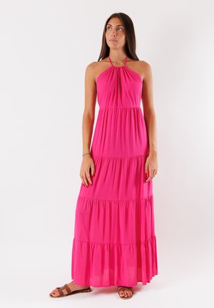 Abito lungo salmone con scollo a halter e volant a strati, realizzato in tessuto leggero. La modella indossa sandali marroni e una collana semplice.