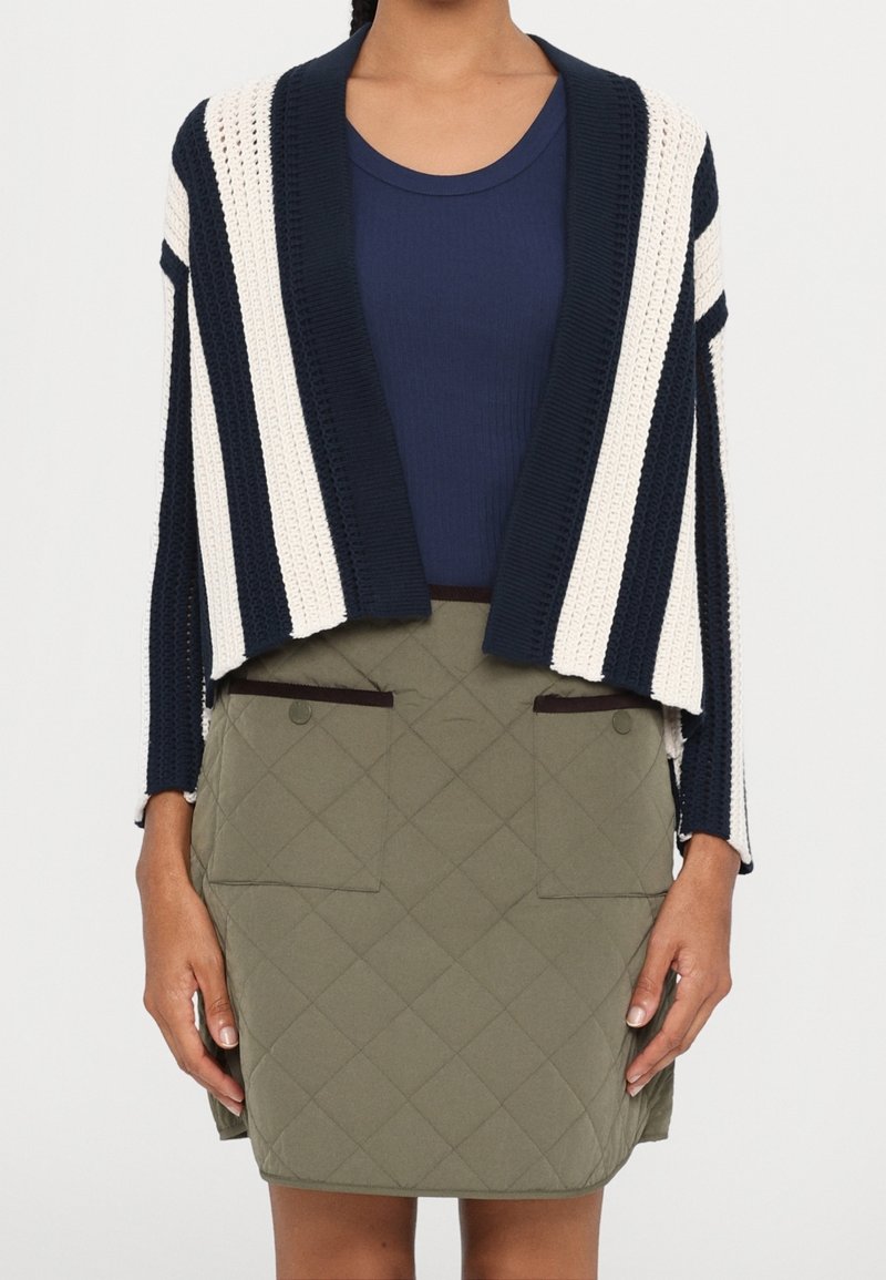 Proužkovaný pletený cardigan v námořnické modři a krémové barvě, doplněný o prošívanou olivově zelenou sukni s velkými předními kapsami a hnědými detaily.