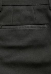 Pantalones de tela negra con una textura suave, que cuentan con un bolsillo trasero y un diseño entallado. La tela presenta un sutil patrón de tejido.
