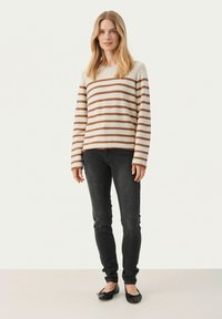Gestreifter Pullover in Creme und Braun, mit langen Ärmeln und rundem Ausschnitt. Kombination mit schwarzen Skinny-Jeans und flachen schwarzen Schuhen.