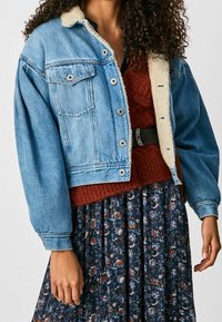 Jeansjacka med fårskinnskrage, med en kortad design, två bröstfickor och ljusblå färg, över en rostfärgad tröja.