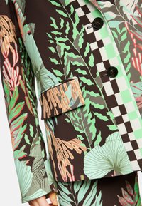 Blazer mit floralem Muster in Grüntönen, Braun und Koralle. Verfügt über schwarze Knöpfe und ein karriertes Stoffdetail am Kragen und an der Tasche.