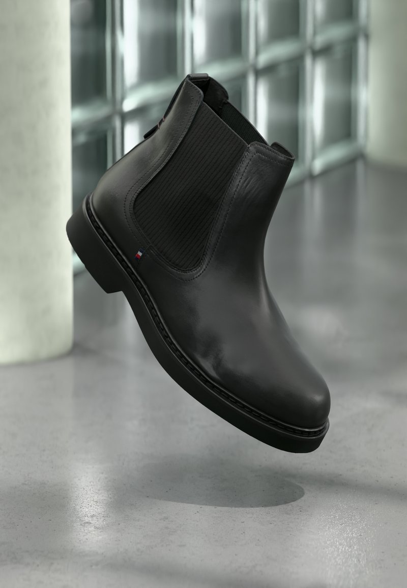 Botim de cano curto em pele preta com painéis laterais elásticos, bico arredondado e sola plana. Logótipo da marca visível na lateral.