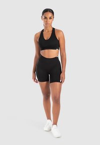 Schwarzes Sportoutfit mit ärmellosem Croptop und hoch taillierter Shorts. Glatte Textur, figurbetontes Design, kombiniert mit weißen Turnschuhen.