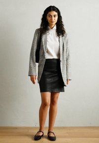 Kockás blazer fekete, fehér és sárga színekben, fehér felsőn, fekete bőr miniszoknyával és fekete lapos cipővel párosítva. Texturált, testre szabott fazon.