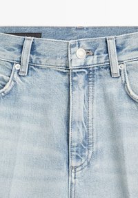 Taille de jean en denim bleu clair avec passants de ceinture, bouton métallique, et bords visibles des poches avant.