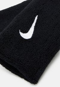 Braccialetto in cotone terry nero con logo Nike ricamato in bianco. Texture morbida con forma tubolare, progettato per l'uso atletico.