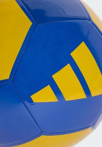 Pallone da calcio blu e giallo con finitura lucida, caratterizzato da un design geometrico e tre strisce gialle su un pannello. Cuciture visibili.