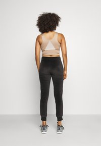 Åtsittande beige sport-bh med en triangulär urtagning, kombinerad med svarta fleece-joggingbyxor och grå sportskor med svarta detaljer.