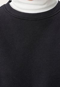 Sudadera negra con cuello redondo acanalado, fabricada en un tejido suave. Presenta un cuello alto blanco debajo, ligeramente visible en el collar.