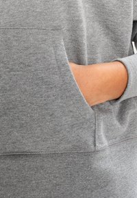 Felpa grigia con tasca. Caratterizzata da una texture morbida e un design semplice. I polsini sono aderenti e il materiale appare essere una miscela di cotone.