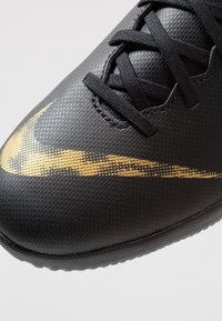Schwarzer Sportschuh mit strukturiertem, synthetischem Obermaterial und goldenem Nike-Swoosh. Verfügt über schwarze Schnürsenkel und eine Gummisohle mit strukturiertem Griff.