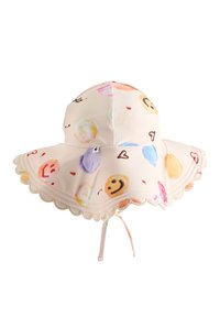 Szeroki kapelusz z miękkiego materiału, z jasnoróżowym tłem i kolorowymi wzorami w uśmiechnięte buźki oraz serca, z falbaniastym brzegiem i paskiem podbródkowym.