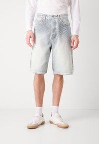 Șorturi din denim cu un aspect deblocat de albastru, caracterizându-se printr-un design clasic cu cinci buzunare și tiv destrămat. Asortate cu adidași albi și șosete de echipă.