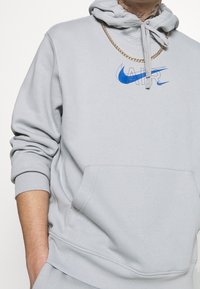 Grå hoodie med framficka, dragsko i huvan och blå Nike "AIR"-logotyp. Har ribbade muddar och mjuk tygtextur.